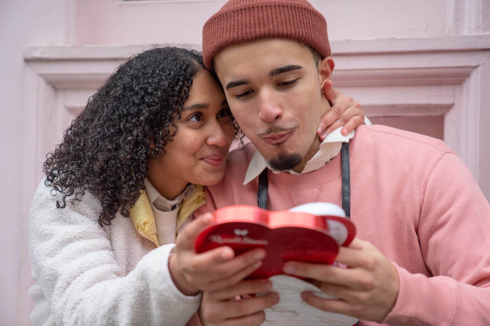 loving young hispanic couple eating chocolates on street and cuddling