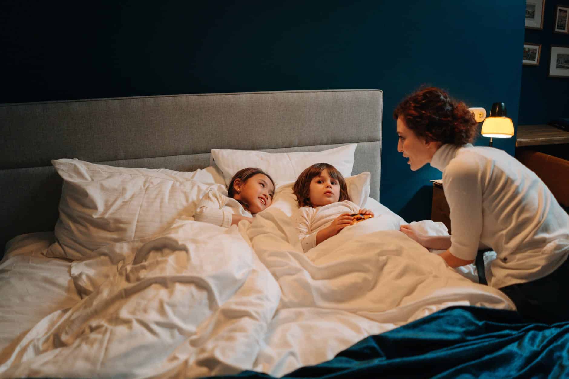 woman telling story to two children in bed