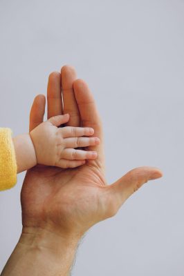 crop person touch palms with newborn baby on gray backdrop