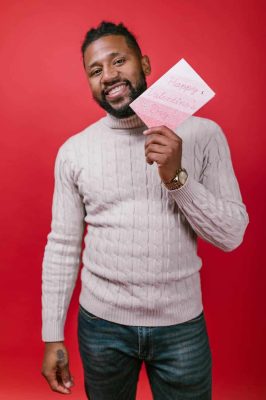 man in white sweater holding a valentine s day card