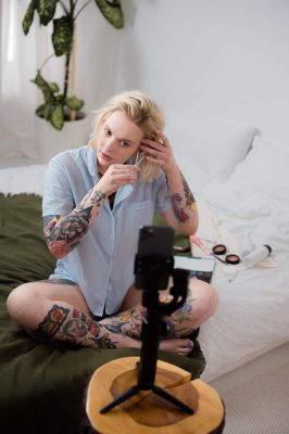 a tattooed woman vlogging on her phone while putting a clip on her hair